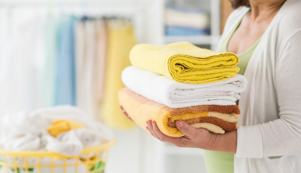 Gramatury ręczników kąpielowych Kobieta z kilkoma ręcznikami składa je po praniu