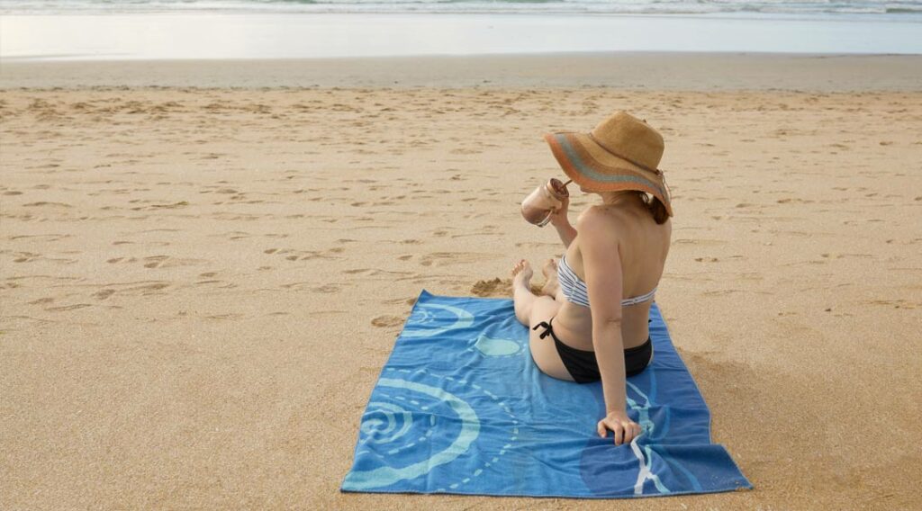 Kobieta pijąca kawę i leżąca na ręczniku plażowym